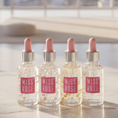 Four clear glass dropper bottles with pink caps and pink MISS ROSE labels, arranged side by side on a light marble surface in a bright indoor setting.